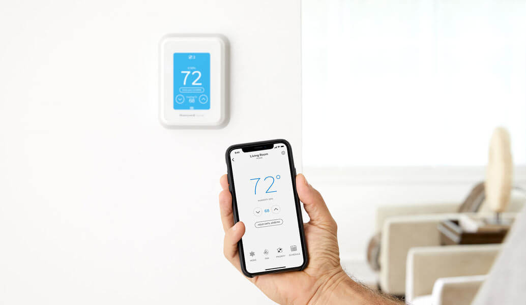 A smart thermostat on the wall and hone own is setting up the temperature on the phone.